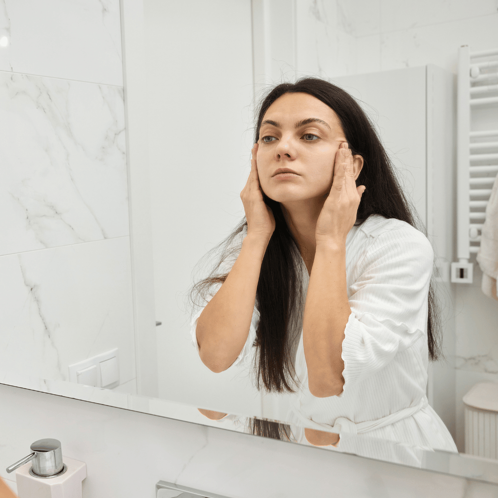 A lady looking into the mirror applying her skincare and getting ready for her LED Face Mask Therapy session