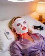 Person wearing a LED face mask in bed with a lamp on a nightstand.