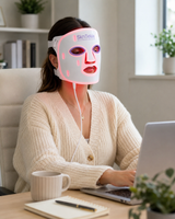 Woman wearing a LED face mask while using a laptop in a home office setting